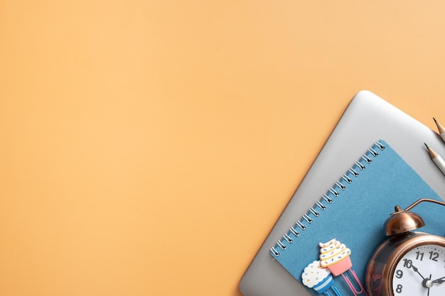 Estacionário colorido e laptop com despertador em fundo colorido Espaço de cópia Espaço de trabalho de crianças vista superior plana lay Conceito de aprendizado on-line