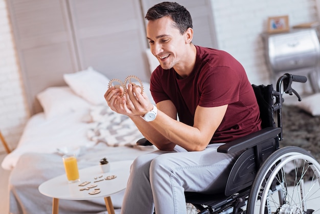 Estado de ánimo alegre. Hombre positivo encantado manteniendo una sonrisa en su rostro y sentado en la silla de ruedas mientras pasa tiempo con placer