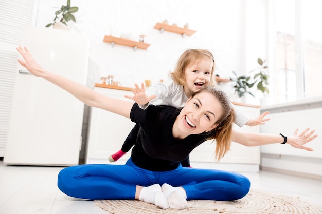 Estado de ánimo juguetón Hermosa madre feliz juega con su hijo haciendo ejercicios deportivos por la mañana