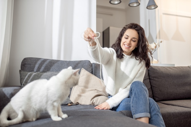 Estado de ánimo juguetón. Hermosa mujer morena jugando con su gato blanco