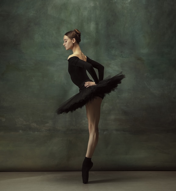 Estado de ánimo místico. Elegante bailarina clásica bailando, posando aislado sobre fondo oscuro de estudio. Tutú negro de elegancia. Gracia, movimiento, acción y concepto de movimiento. Parece ingrávido, flexible. De moda.