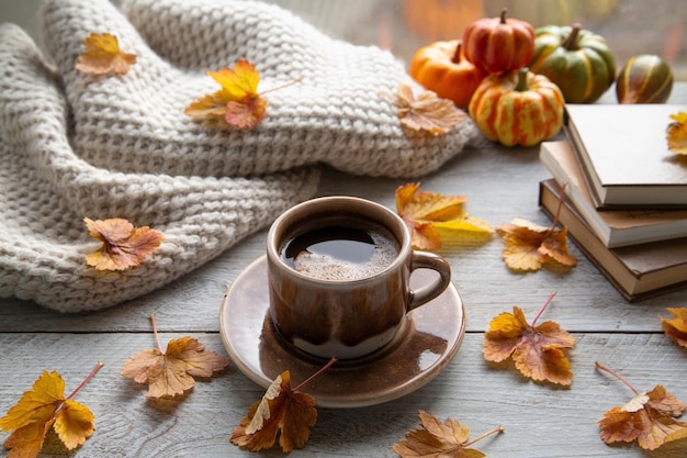 Estado de ánimo otoñal ambiente otoñal Una taza de café una bufanda tejida libros y hojas de otoño en el alféizar de la ventana