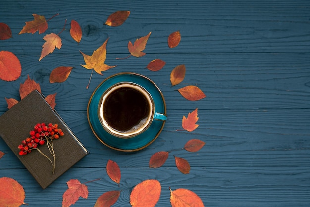 Estado de ánimo otoñal fondo otoñal Una taza de café un libro hojas brillantes y bayas en una mesa de madera oscura Vista superior con espacio de copia