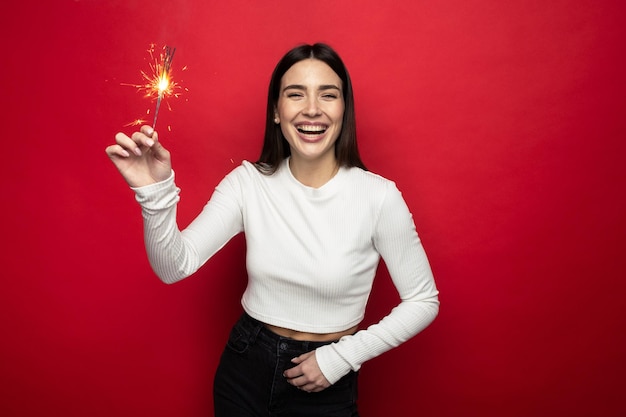 Estado de ánimo de vacaciones - mujer joven sonriente en un suéter blanco con luces de bengala