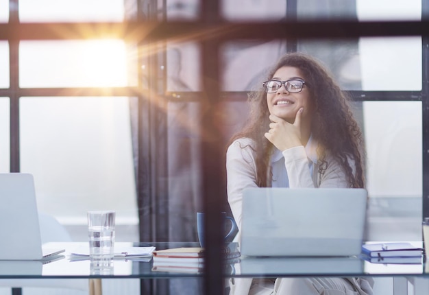 Estagiária morena de óculos senta-se com um laptop em uma mesa no escritório