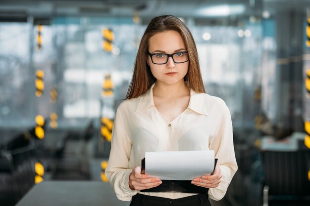 Estagiário workaholic. espaço de trabalho de escritório vazio. jovem de óculos com documentos, olhando diretamente para a câmera.