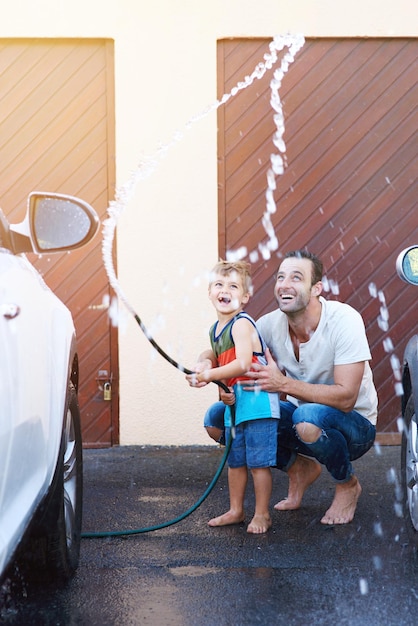 Se están divirtiendo mucho Toma completa de un padre y su hijo jugando con una manguera mientras lavan un auto juntos