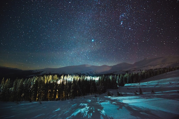 Estância de esqui europeia com vapor e fumaça, localizada entre as pitorescas colinas da montanha da floresta à noite contra um lindo céu estrelado. conceito de férias de inverno. copyspace