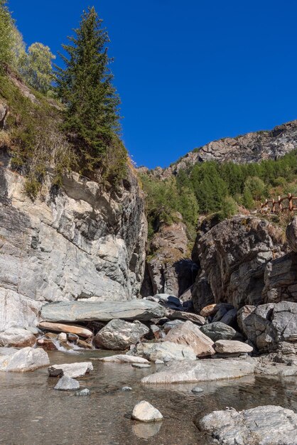 Estanque escénico de agua clara sendero de barandilla de madera por Lillaz Catarata vertical Cogne Aosta Italia