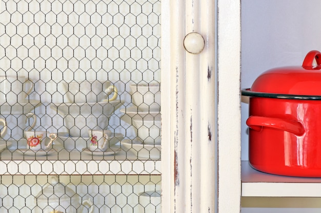 Estante de armario de cocina blanco con tazas de té y café también blancas, destacando una olla roja