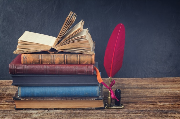 Foto estante de madeira com pilha de livros antigos e caneta de pena vermelha em tons retrô