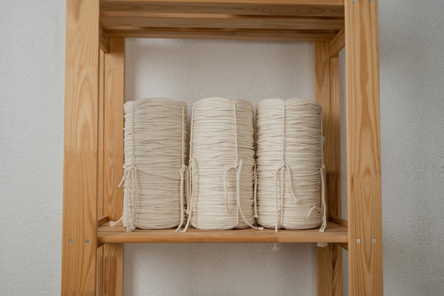 Estantería de madera con rollos de cuerda blanca sobre un fondo de pared blanco