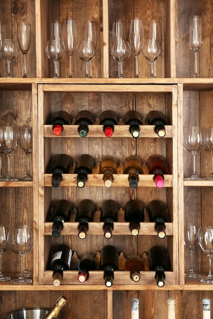 Foto estanterías con botellas de vino y vasos sobre un fondo de pared de madera