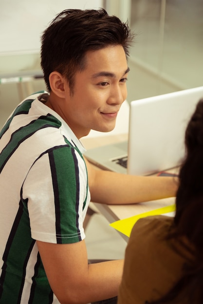 Estar en todos los oídos. Hombre asiático alegre manteniendo una sonrisa en su rostro mientras escucha a su tutor