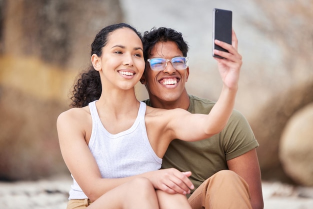 Estaré a tu lado a través de cualquier cosa Foto de una pareja joven tomándose una selfie en la playa