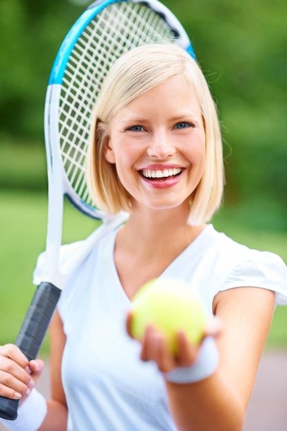 ¿Estás listo para un juego? Retrato de una joven jugadora de tenis sosteniendo su raqueta y ofreciéndote la pelota.