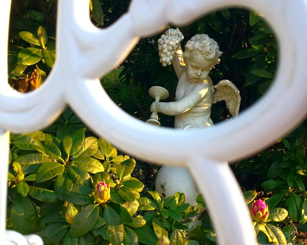 Foto estatua de ángel en medio de plantas en el jardín vista a través de la valla