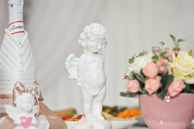 Estatua de un angelito blanco sobre la mesa entre las flores 1855