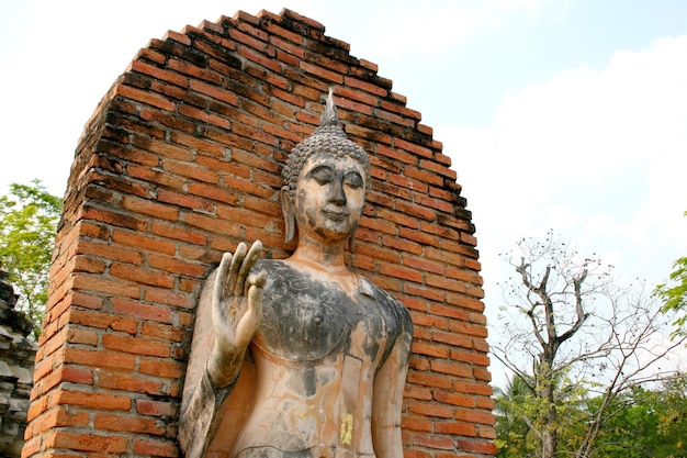 Una estatua de Buda se encuentra frente a una pared de ladrillos.