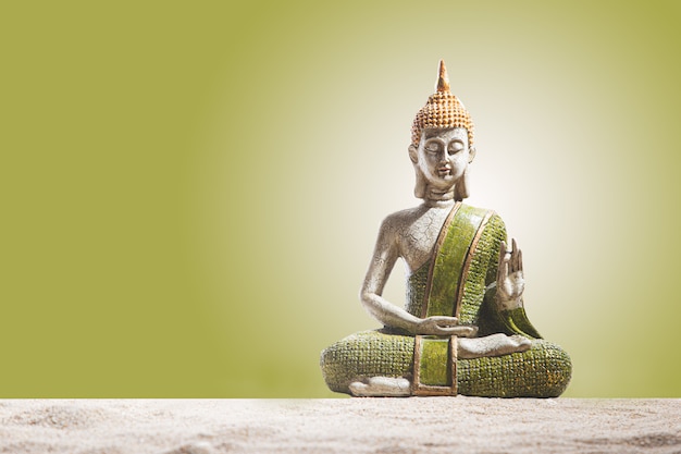 Estatua de Buda verde y dorado, sobre arena. Meditación, espiritualidad y concepto zen.