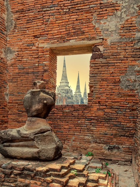 Estátua de Buda quebrada perto da parede de tijolos com vista de três pagodes ou chedis antigos atrás do templo Wat Phra Si Sanphet na cidade histórica de Ayutthaya, Tailândia