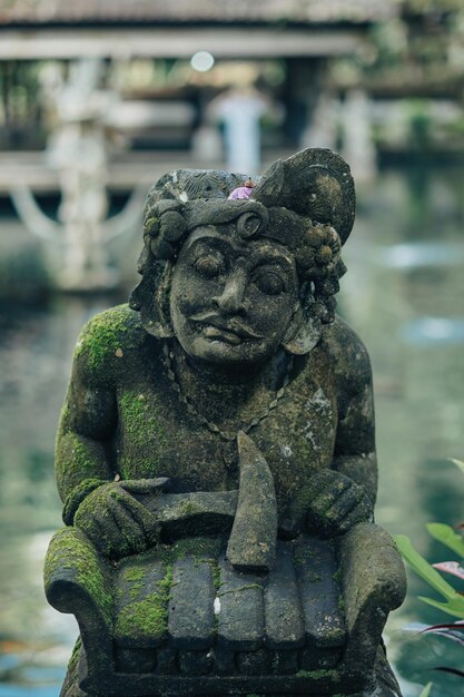 Estátua de pedra balinesa dwarapala no lago de peixes koi