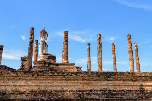 Estátua do Buda antigo sentado entre os pilares das ruínas sob o céu azul em Wat Maha. Aquele templo no Parque Histórico de Sukhothai é uma cidade antiga e atrações famosas, Tailândia