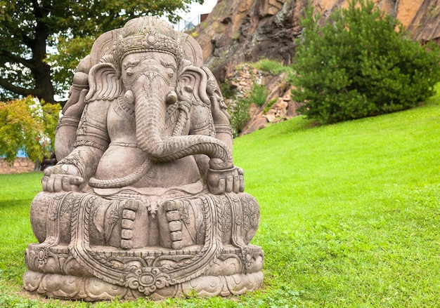 Estatua de Ganesha, hecha de piedra, con un hermoso jardín de montaña en segundo plano.