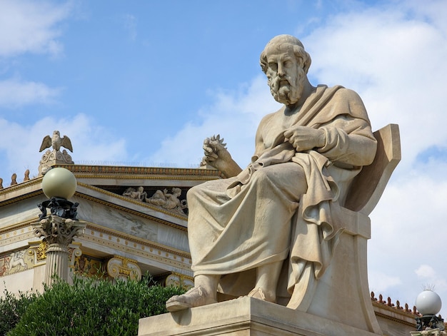 Una estatua de un hombre con un libro en la mano se sienta frente a un edificio.