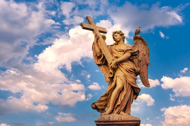 Estatua de mármol del ángel con la cruz al atardecer, uno de los diez ángeles en el puente de San Ángel, símbolos de la Pasión de Cristo, Roma, Italia