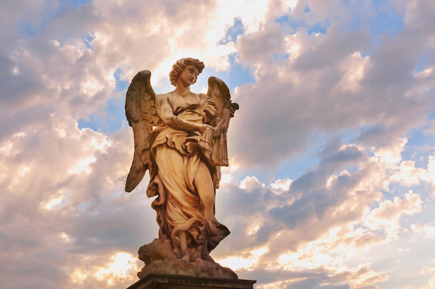 Foto estatua de mármol del ángel con los látigos al atardecer, uno de los diez ángeles en el puente de san ángel, símbolo de la pasión de cristo, roma, italia