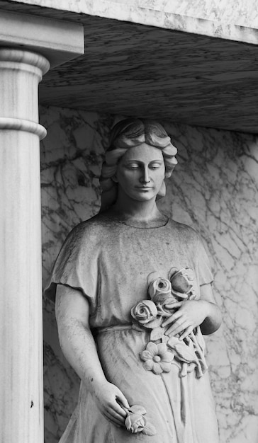 Una estatua de una mujer con flores en las manos está debajo de un pilar.