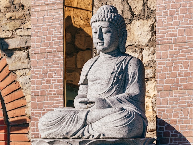 Estatua de piedra blanca de un Buda sobre fondo de mampostería