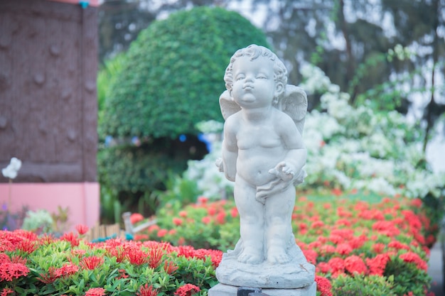 Estatua de piedra de Cupido en el jardín de flores.