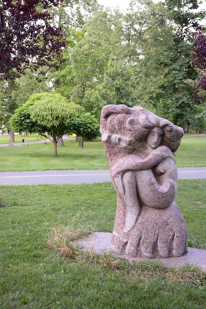 Estatua de piedra de una niña en un parque de verano con el telón de fondo de árboles, césped y caminos