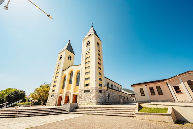 estatua de la Santísima Virgen María sosteniendo una rosa roja mientras la Iglesia de Santiago en Medjugorje