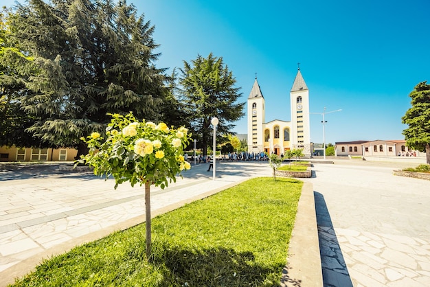 Foto estatua de la santísima virgen maría sosteniendo una rosa roja mientras la iglesia de santiago en medjugorje