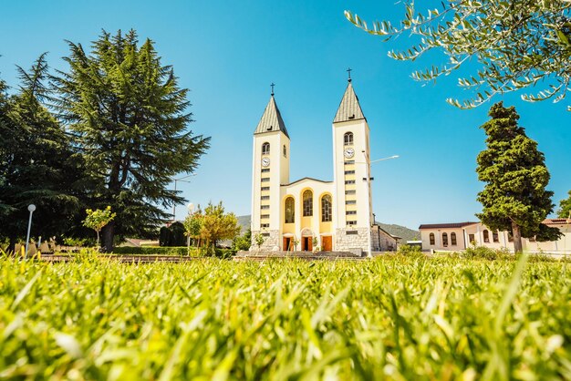 Foto estatua de la santísima virgen maría sosteniendo una rosa roja mientras la iglesia de santiago en medjugorje