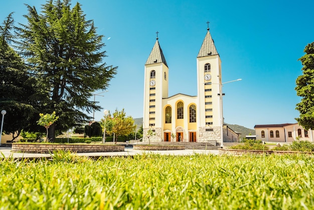 Foto estatua de la santísima virgen maría sosteniendo una rosa roja mientras la iglesia de santiago en medjugorje