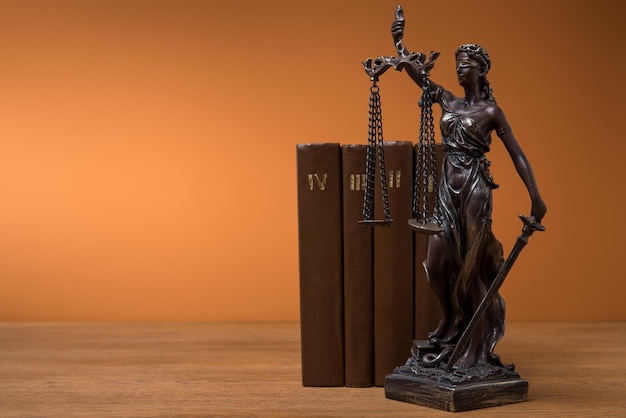 Estatueta de bronze com balança da justiça e fileira de livros marrons na mesa