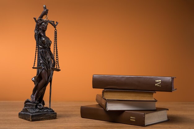 Foto estatueta de bronze com balança da justiça e volumes de livros marrons na mesa