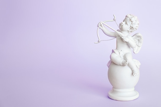 Estatueta de um anjo Cupido com um laço em um fundo roxo. Dia dos namorados.