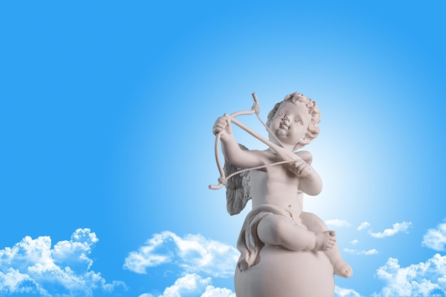 Foto estatueta de um anjo cupido no pódio com um arco e flecha em um céu azul com nuvens de fundo dia dos namorados