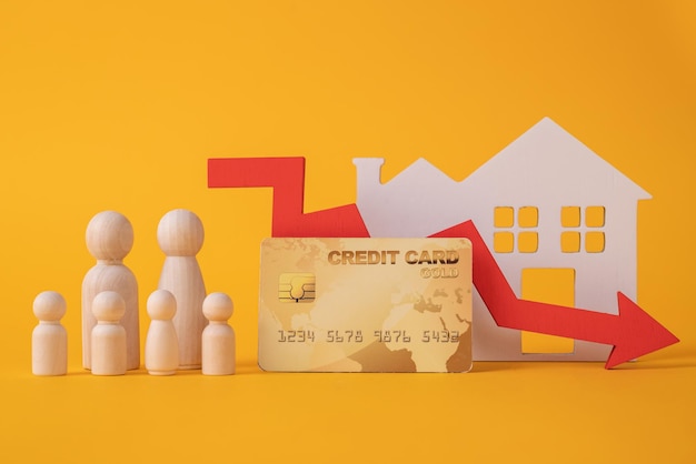 Estatuetas de madeira de uma família e um cartão de crédito com uma seta para baixo ao lado de uma casa branca O conceito de redução de um empréstimo à habitação a uma jovem família numerosa