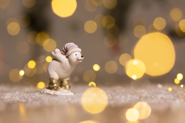 La estatuilla de un cachorro de oso blanco sostiene una bola de nieve detrás de la decoración festiva, cálidas luces bokeh.