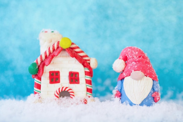 Estatuilla de tarjeta de Navidad de un gracioso gnomo y una casa de pan de jengibre en la nieve sobre un fondo azul.