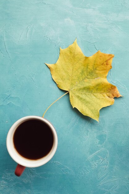 Esté caliente con café negro en otoño. Hoja de arce en la pared azul