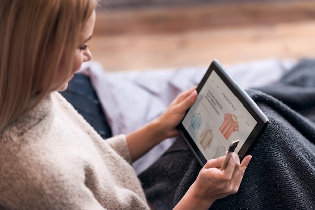 Esteja na moda. Mulher bonita jovem alegre desfrutando de compras online e usando o tablet e cartão de crédito enquanto está sentado na cama.