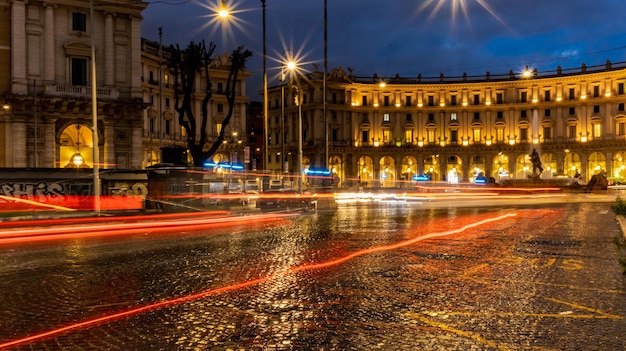 Estelas de luz de coches en la plaza de la tarde en Roma después de la lluvia Rutas de tráfico nocturno Desenfoque de movimiento