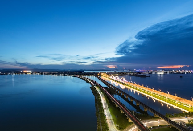 Estelas de luz en el ferrocarril y el puente de carretera la noche cae sobre el lago en la ciudad de jiujiang China